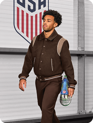 U.S. Soccer player Tyler Adams carries a custom blue, silver, and green dopp kit shaped like a soccer cleat.