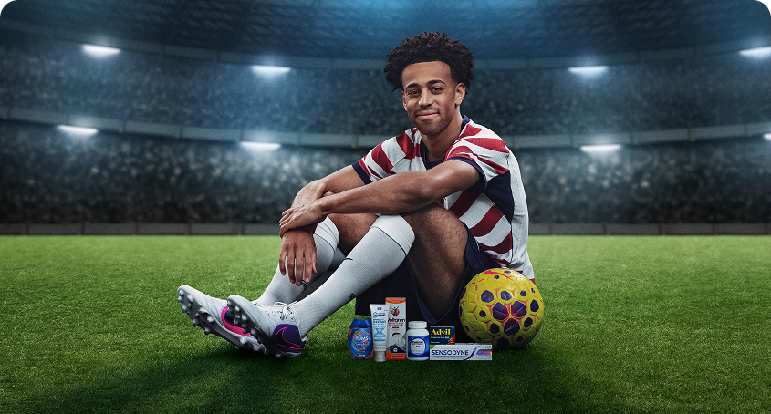 Soccer Player Tyler Adams sits on a field next to a soccer ball and Haleon products. Disclaimer text reads: Some products may contain NSAIDs and/or Acetaminophen and should not be taken together. Please review labels and use as directed.