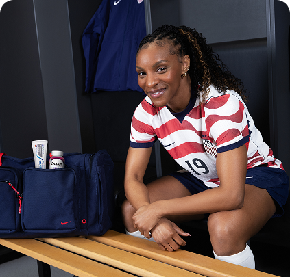 Former U.S. Soccer player Crystal Dunn sits in a locker room, with
Sensodyne and Centrum products visible in her
bag.