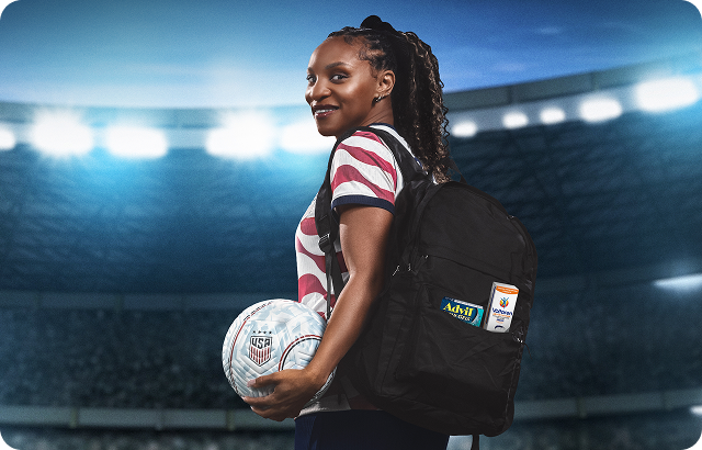 Former U.S. Soccer player Crystal Dunn stands inside a stadium with Advil and Voltaren products in her bag. Disclaimer says Some products may contain NSAIDs and/or Acetaminophen and should not be taken together. Please review labels and use as directed.