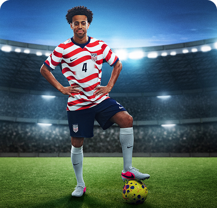 U.S. Soccer player Tyler Adams stands on a soccer field, hands on his hips and foot on a ball.