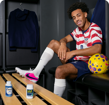 U.S. Soccer player Tyler Adams sits in a locker room with his foot on a bench, next to a package of Centrum and Advil.