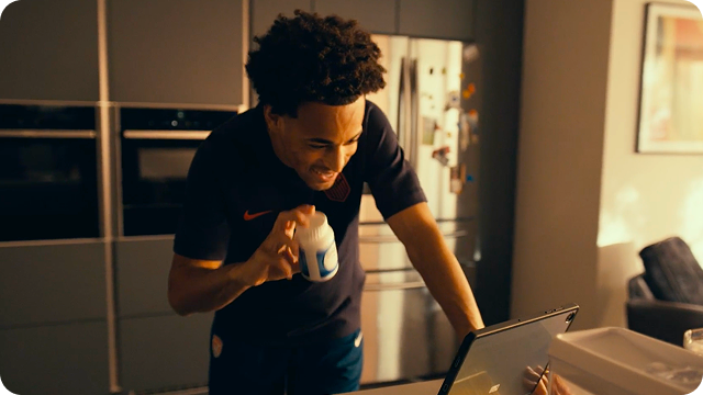 U.S. Soccer player Tyler Adams standing in his kitchen, holding up a bottle of Centrum. An overlay with a play video button appears in the corner.