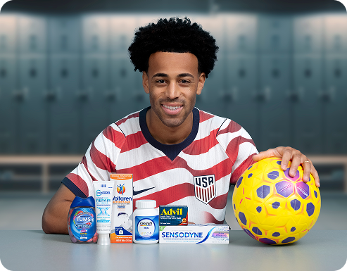 Soccer player Tyler Adams poses in a locker room with a ball and several Haleon products. A U.S. Soccer Logo reads Official Partner of U.S. Soccer, and a disclaimer reads Some products may contain NSAIDs and/or Acetaminophen and should not be taken together. Please review labels and use as directed.