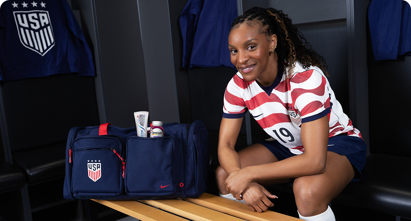 Former U.S. Soccer player Crystal Dunn sits in a locker room, with Sensodyne and Centrum products visible in her bag.