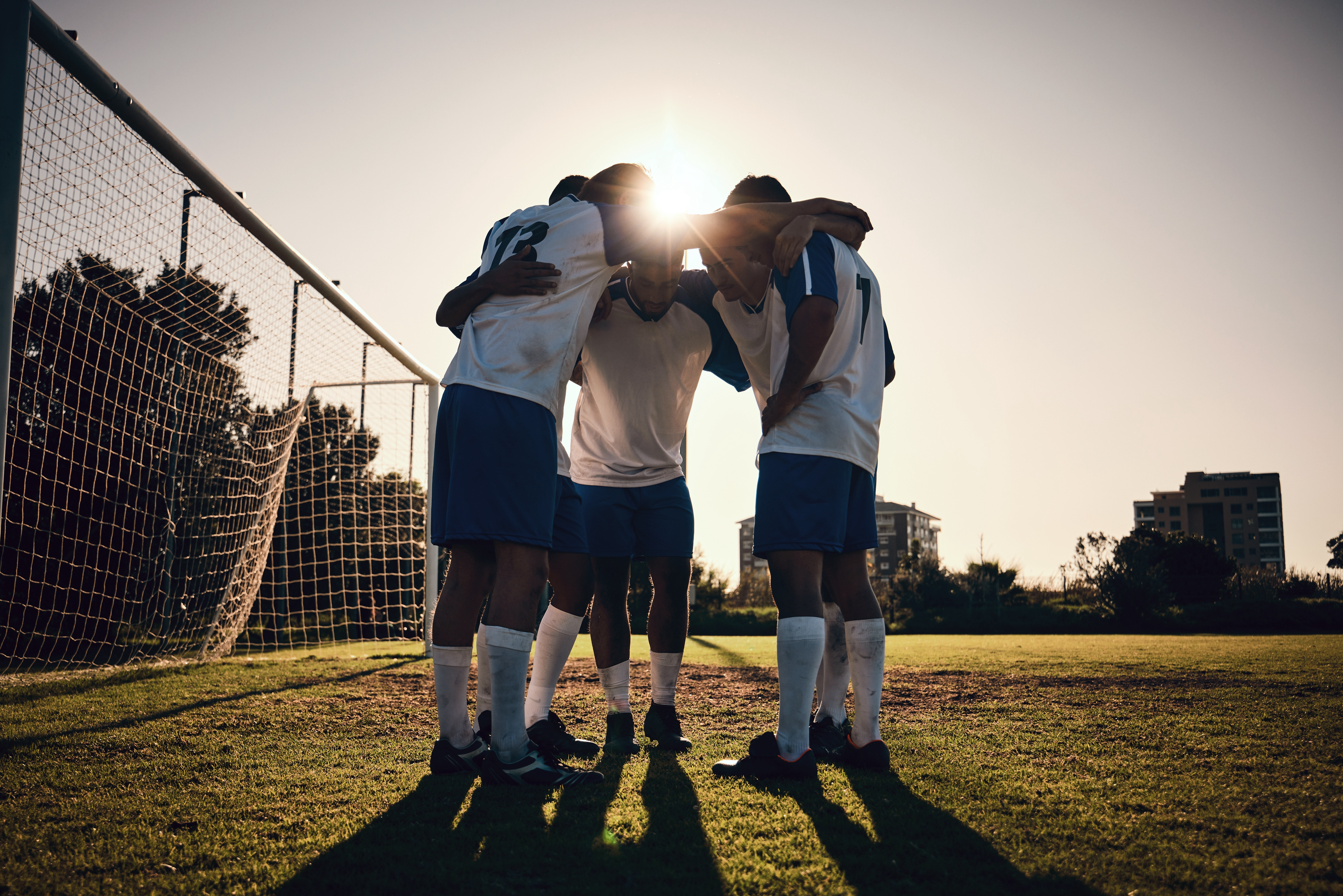 Soccer team in a huddle near a goal.