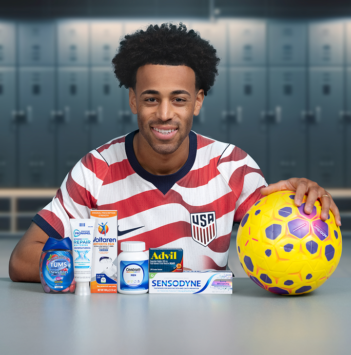 Soccer player Tyler Adams poses in a locker room with a ball and several Haleon products. A U.S. Soccer Logo reads Official Partner of U.S. Soccer, and a disclaimer reads Some products may contain NSAIDs and/or Acetaminophen and should not be taken together. Please review labels and use as directed.