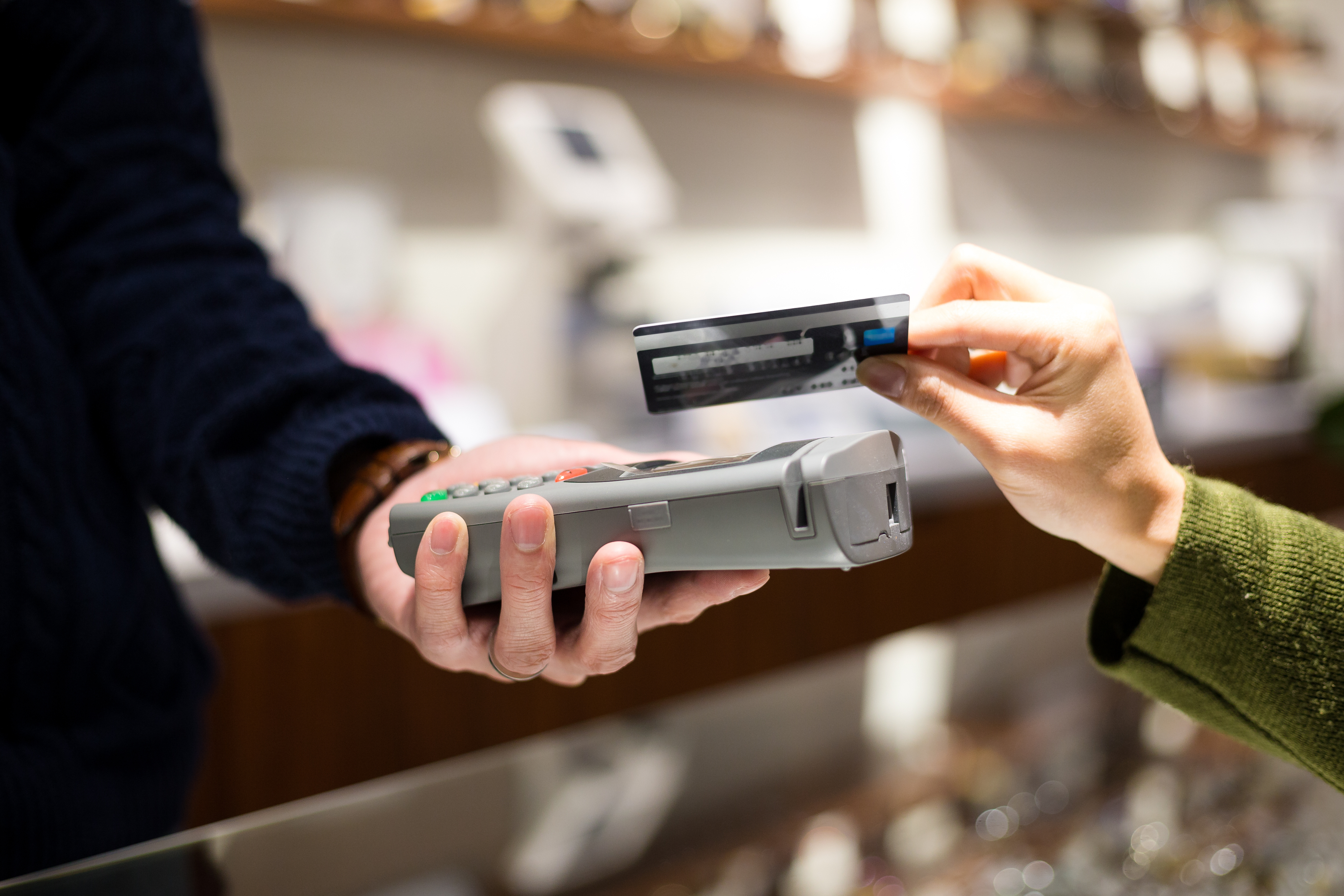 Hand holding a card reader as another hand taps a credit card on top