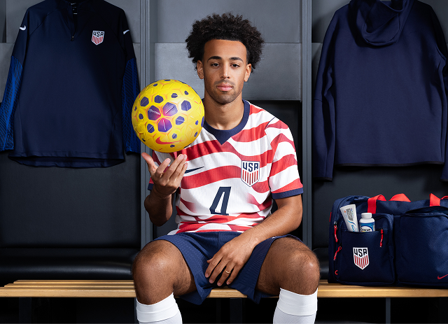 U.S. Soccer player Tyler Adams sits in a locker room, holding a soccer ball.